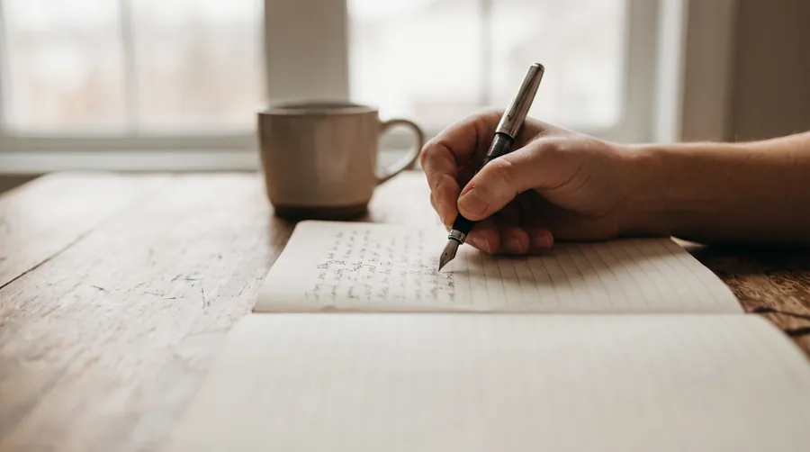 Close-up of hand writing gratitude journal entry on lined notebook paper