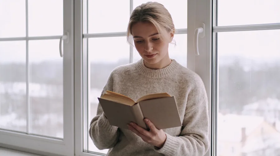 a person reading by a window on a grey winter afternoon during a focused season